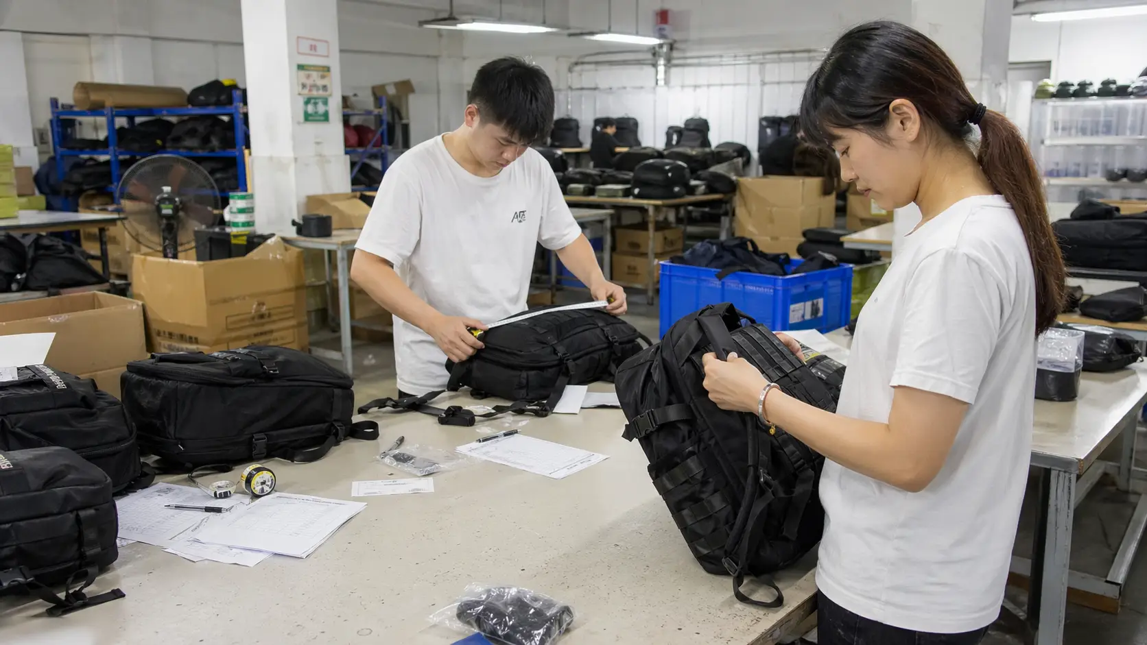 Quality inspection of finished custom backpacks, two workers measuring and checking backpacks before packing