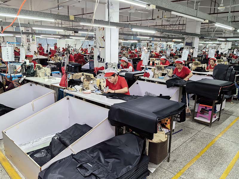 Sewing workshop making custom tool bags and backpacks, workers in red uniforms at rows of industrial sewing machines